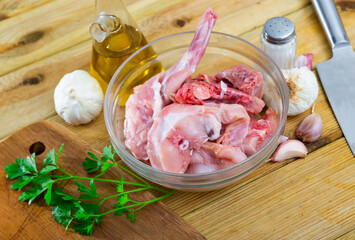 Raw sliced rabbit lying in glass bowl with fresh parsley sprigs, garlic, oil and spices. Dietary...