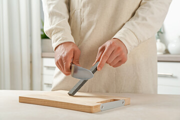 Man sharpening knife with sharpener at beige table indoors, closeup