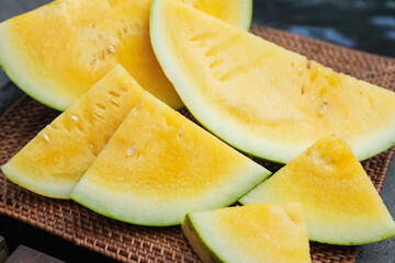 Pieces of ripe yellow watermelon on wicker table near swimming pool, closeup