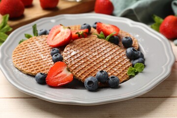 Tasty Dutch waffles (stroopwafels), mint and berries on light wooden table, closeup