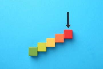 Maximum. Colorful cubes and arrow pointing at red one on light blue background, flat lay