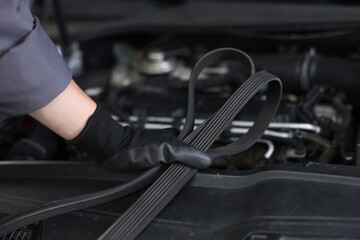 Auto part. Professional mechanic with timing belt near open hood of car indoors, closeup