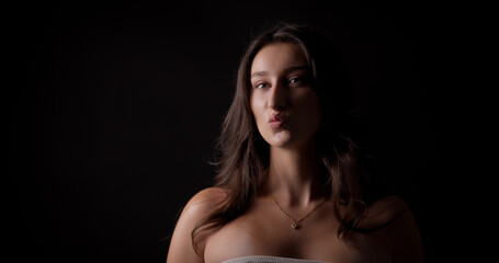 Studio portrait of a young woman puckering her lips on a black background