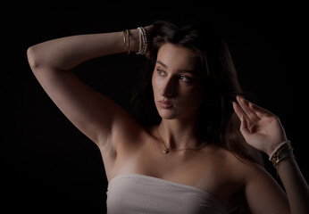 Studio portrait of a young woman posing with hand in hair and arm raised on a black background