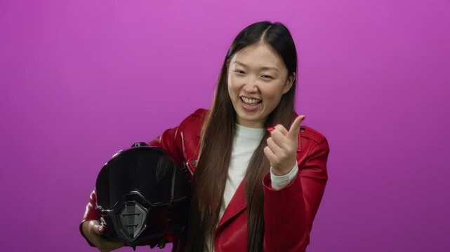 Woman posing confidently in red jacket holding helmet against vibrant pink background showcasing modern style and energy