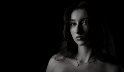 Black and white portrait of a young woman with long hair and bare shoulders, wearing a necklace...