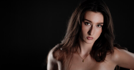 Naklejka premium Studio portrait of beautiful young woman with long brown hair wearing a golden necklace, posing on black background