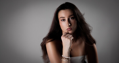 Studio portrait of a young woman with long brown hair resting her chin on her hand
