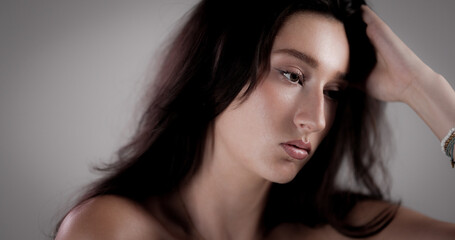 Portrait of a beautiful pensive young woman with long brown hair touching her head with hand and...