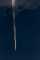 Trail of the plane in the dark sky with white clouds.