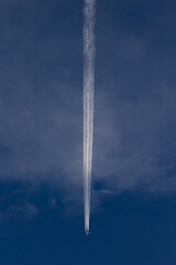 Trail of the plane in the dark sky with white clouds.