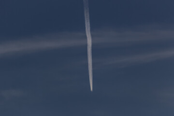 Trail of the plane in the dark sky with white clouds.
