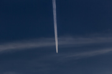 Trail of the plane in the dark sky with white clouds.