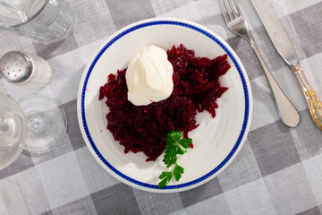 Fresh beetroot salad served on plate and decorated with parsley sprig and sour cream.