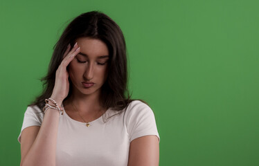 Young woman suffering from headache touching her forehead on green screen background