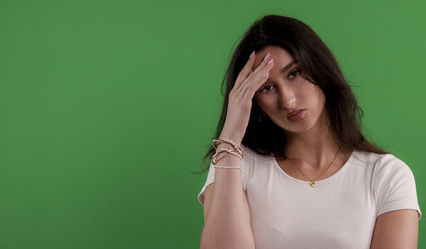Young woman suffering from headache touching her forehead with hand on green background