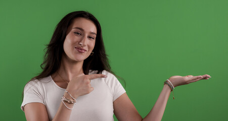 Young woman pointing at her open hand showing something on a green screen background