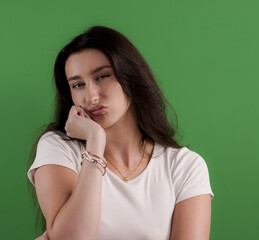Portrait of a bored young woman resting her face on her hand against a vibrant green chroma key...