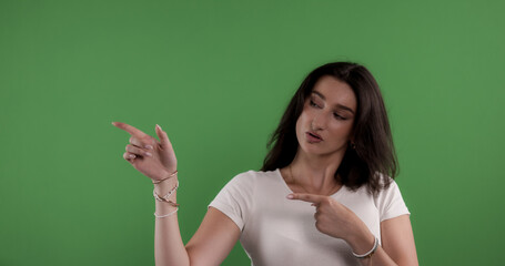 Young woman pointing with index fingers to the side and down on green screen background