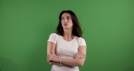 Thoughtful young woman crossing arms and looking up with an upset facial expression against chroma...