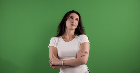 Studio shot of a thoughtful young woman with crossed arms, looking up and thinking against a chroma...