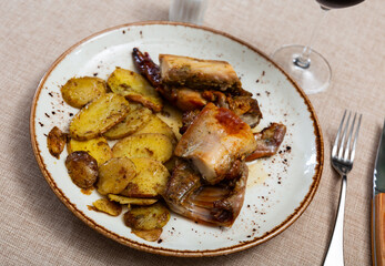 Lunch is served on plate - pieces of young rabbit baked with slice of potato. Close-up, top view