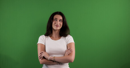 Studio portrait of a young woman smiling and thinking with arms crossed against a chroma key...