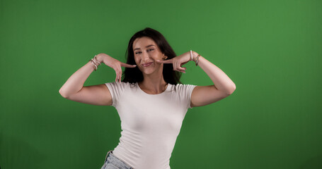 Young woman pointing her cheeks with index fingers, smiling on chroma key background