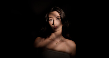 Studio portrait of a young woman with long brown hair and bare shoulders, illuminated by stripes of light against a dark background