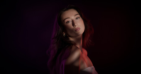 Studio portrait of beautiful young woman with long hair posing under colorful neon lights