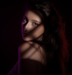 Fashion portrait of a beautiful young woman with long brown hair, illuminated by a purple light,...