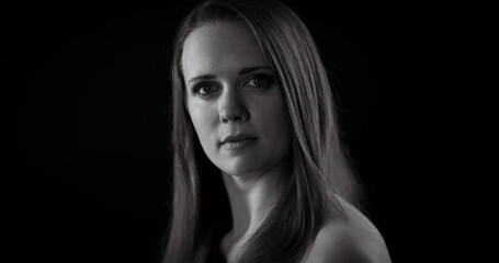 Black and white portrait of a serious young Caucasian woman with long hair posing in the studio