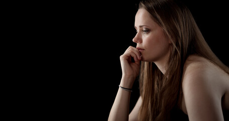 Fototapeta premium Sad woman with hand on chin is looking down and thinking about something on black background