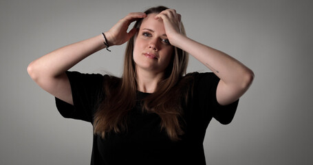 Studio portrait of a young woman wearing black t shirt touching her hair with both hands on a gray...