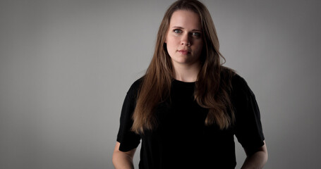 Studio portrait of a serious young woman with long brown hair wearing black t shirt on a gray...