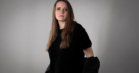 Studio portrait of a young woman with long brown hair, wearing a black t shirt and jacket, posing...