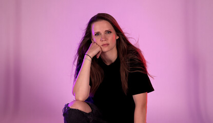 Studio shot of a young woman with long brown hair, wearing a black t shirt and ripped jeans, posing...