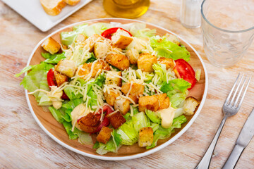Portion of fresh Caesar salad with tomatoes served on plate in restaurant.