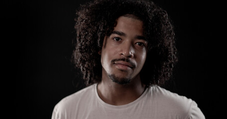 Young African American man with curly hair and goatee posing on black background