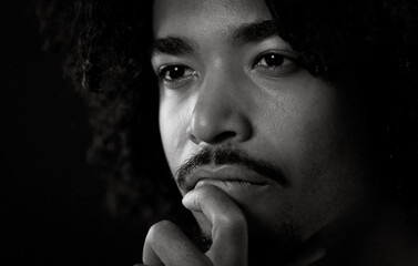 Close up portrait of a thoughtful young African American man with curly hair and mustache, holding...