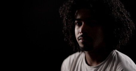 Portrait of serious young african american man with curly hair posing in dark room