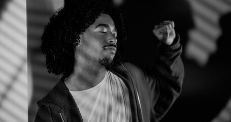 Portrait of a young man with curly hair dancing with closed eyes and raised fist in black and white