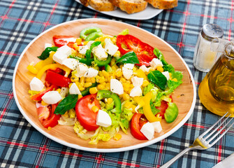 Popular all over the world appetizing vegetable salad made of tomatoes, Feta cheese, lettuce leaves, canned corn and pepper
