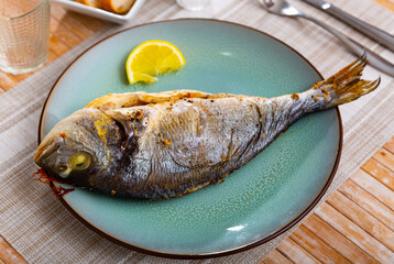 Appetizing baked dorada fish served on platter with slice of lemon