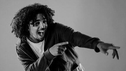 Black and white portrait of a young man with curly hair pointing his fingers and screaming
