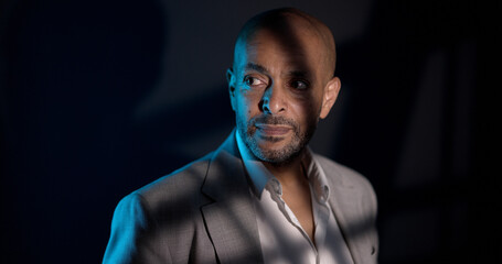 Portrait of a serious african american businessman looking away in a dark room with blue light...