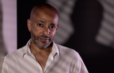 Portrait of a confident african american businessman posing in white shirt in a room with shadows...