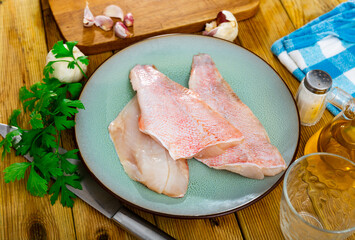 Three pieces of raw sea bass fillet on a plate while cooking in a home kitchen with a sprig of...