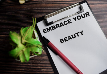 Concept of embrace your beauty write on clipboard isolated on Wooden Table.
