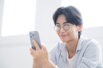Fototapeta premium 逆光の綺麗な部屋でスマホを見る、持つ眼鏡のハンサムな男性のクローズアップ 